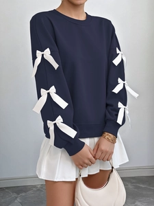 Detail of dark blue sweatshirt featuring white ribbon bows on long sleeves