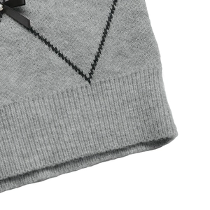 Detail of grey knit sweater showing black argyle patterns and a ribbon bow with pearl