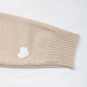 Detailed view of beige ribbed knit cuff featuring a white embroidered heart patch