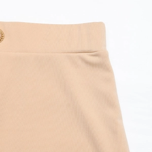 Close-up of beige ribbed knit skirt waist with textured fabric and gold button detail