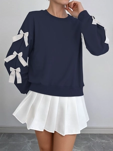 Detail of three white 3D bows on the sleeve of a navy blue crewneck sweatshirt