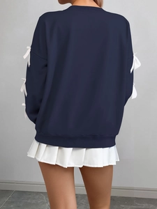 Detail of navy sweatshirt featuring white bow accents on sleeves and ribbed hem design