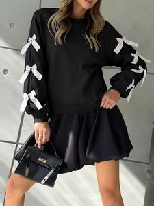 Detail view of black crewneck sweatshirt featuring white silk bows on long sleeves