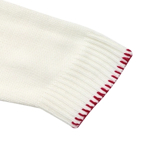 Close-up of white knit sweater cuff with ribbed texture and red contrast stitching detail