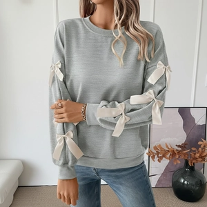 Detail of light grey sweatshirt sleeves featuring symmetric cream satin bow accents