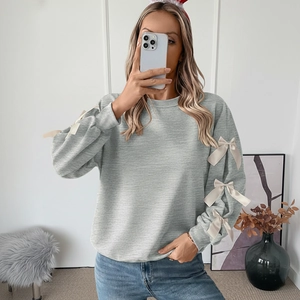 Detail of grey crewneck sweatshirt featuring cream silk bows on long sleeves