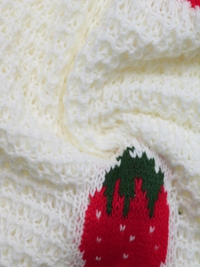 Close-up of soft white knit fabric featuring red and green strawberry jacquard patterns