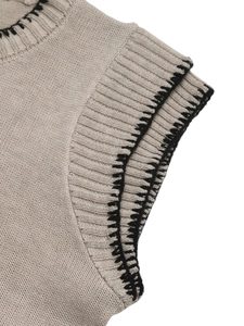 Close-up detail of beige knit top featuring black contrast stitching and ribbed neck line
