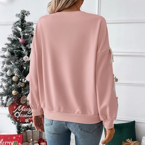Detail of pink Christmas sweatshirt with white bow accents on sleeves in festive setting