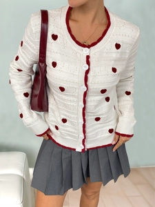Detail of red heart jacquard pattern and ribbed edges on white knit cardigan sweater