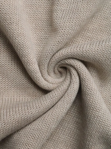 Macro shot of beige knitted fabric texture showing soft stitch patterns and draping