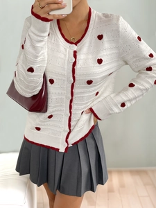 Detailed close-up of white knit cardigan with red heart patterns and contrast red trim
