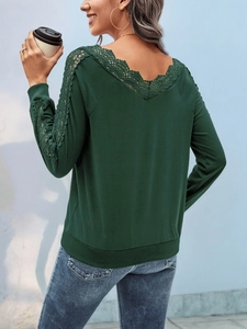 Detail of dark green V-back top featuring elegant lace patchwork and ribbed cuffs