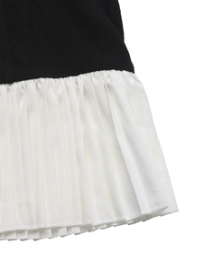 Detail of contrast stitching and pleated white hem on a black two-piece dress
