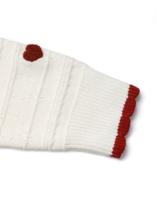 Detail of ribbed cuff with a red heart patch and crocheted wave trim on a knit cardigan