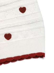 Detail of white knit cardigan showing red heart patterns and scalloped embroidery edges