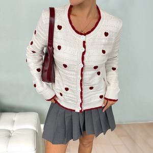 Elegant white knit cardigan with red heart patterns and contrasting crochet trim details