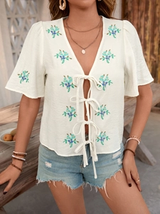 Detail of bohemian summer blouse with floral embroidery and ribbon tie closures