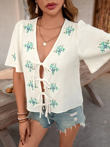 Close-up of white summer blouse with floral embroidery and decorative front bow ties