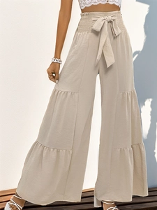 Detail of tiered wide-leg high-waisted beige trousers with a matching fabric bow belt