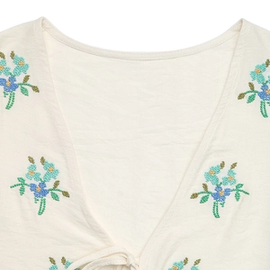 Close-up of V-neck neckline featuring blue floral embroidery and bow tie closure