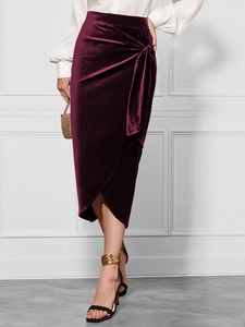 Detail of burgundy velvet midi skirt featuring a waist tie knot and asymmetrical slit