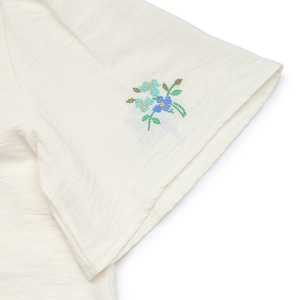Detail of cream-colored shirt cuff with delicate blue floral embroidery and linen texture