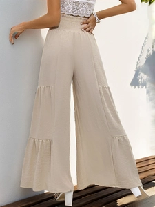 Detail of high-waist beige tiered trousers with elastic waistband and pleated texture