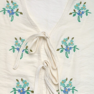 Detailed view of floral embroidery and bow tie closures on an ivory summer shirt