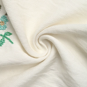 Close-up of white sheer fabric with green leaf embroidery and horizontal texture details
