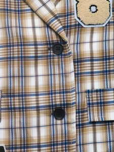 Detail eines karierten Blazers mit braunem Karomuster, Knöpfen und Plüschbär-Patch