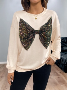 Detail of light peach sweatshirt featuring a large bow made of colorful sequins