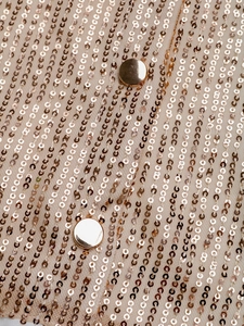Macro shot of sparkling champagne gold sequins and metallic buttons on a sheer long sleeve shirt