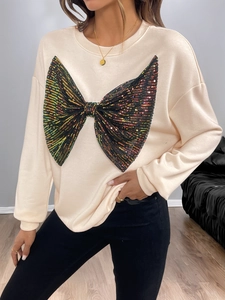 Close-up of oversized black sequin bow detail on a beige long-sleeved sweatshirt