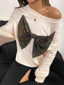 Detail of a beige off-shoulder sweatshirt featuring a large iridescent sequin bow design