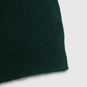 Détail de la texture en maille gaufrée vert foncé et de l'ourlet côtelé du pull