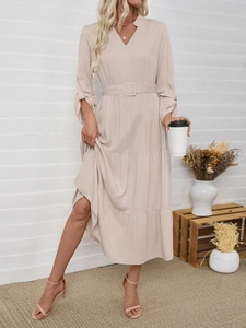 Detail view of the beige V-neck dress featuring a layered skirt and square buckle belt