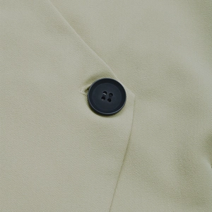 Detailed macro view of a black four-hole button on the beige woven blazer fabric