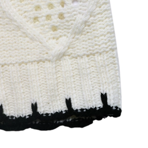Dettaglio maglione a maglia grossa color crema con bordo smerlato nero e trama a coste a V