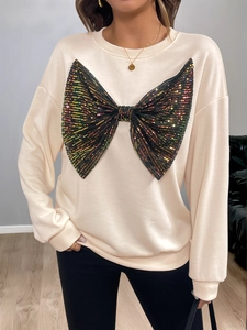 Close-up of sparkling black sequin bow detail on a cream oversized crewneck sweatshirt