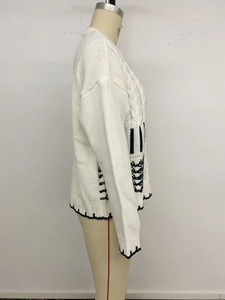 Dettaglio di maglione bianco a trecce con strisce nere e motivi a zigzag sul fianco