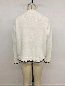Dettaglio di maglione bianco a maglia grossa con ricamo a smerlo nero sull'orlo