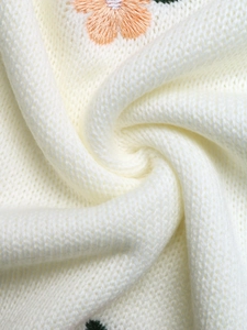 Detailed macro view of cream knitted fabric with orange floral embroidery and green leaves