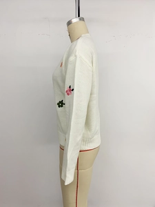 Detailed embroidery of colorful flower patterns on a white knit sweater with ribbed cuffs