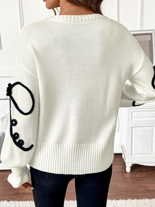 Détail du pull en maille blanc avec cordons noirs aux manches et ourlet côtelé