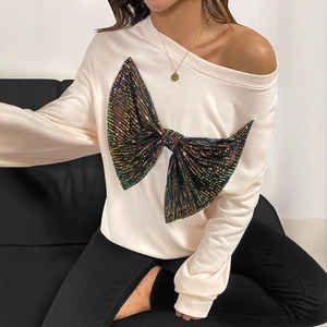 Beige off-shoulder sweatshirt featuring a large colorful sequin bow and relaxed fit