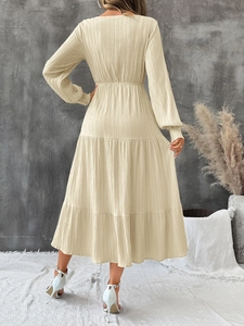 Back view of a beige V-neck maxi dress featuring textured fabric and tiered skirt detail