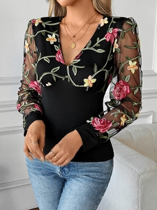 Close-up of V-neck mesh sleeves with intricate floral embroidery on a black top
