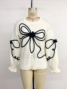 Détail pull en maille blanc avec applique nœud noir 3D et finitions côtelées
