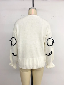 Détail des manches de pull blanc avec lignes noires en relief et poignets à volants